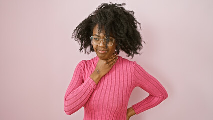 An attractive african american woman in a pink sweater poses indoors with a thoughtful expression.