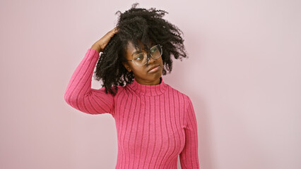 A contemplative african american woman in glasses posing indoors against a pink background.