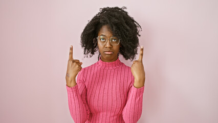 African adult woman in pink sweater pointing upwards, wearing glasses with a neutral background