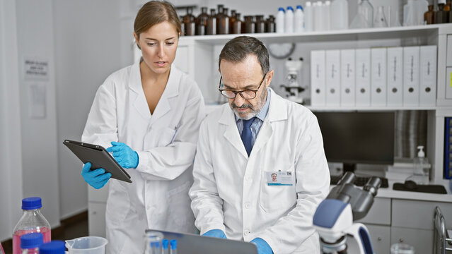 Two brooding scientists huddled together at their lab, engrossed in serious research on their laptop and touchpad, making breakthroughs in science, medicine and biology.