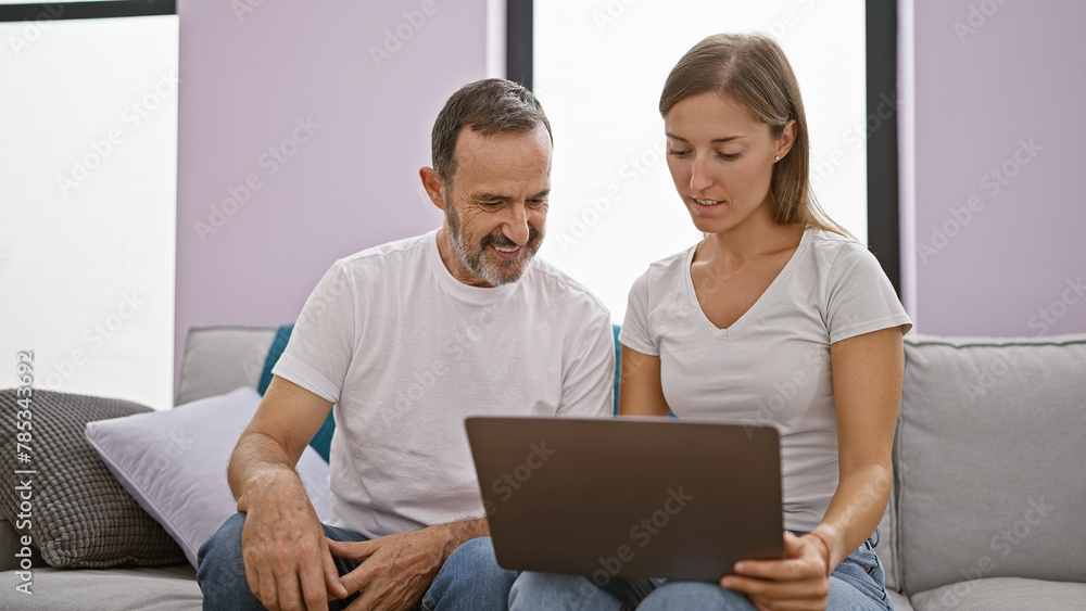 Poster Confident father and smiling daughter enjoying online fun on laptop, sitting together on indoor sofa at home in a relaxed lifestyle, expressing love and positive family relationship.