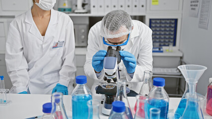 Two scientists wearing medical mask and gloves using microscope at laboratory