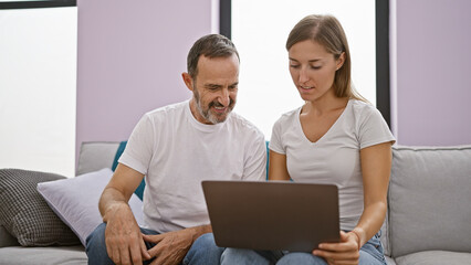 Confident father and smiling daughter enjoying online fun on laptop, sitting together on indoor...