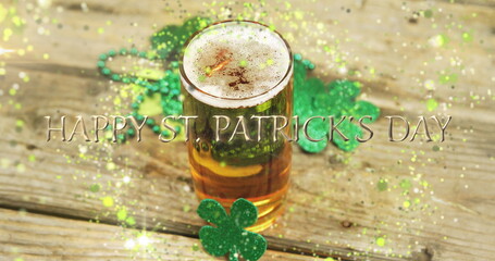 Image of st patrick's day text, shamrock and glass of beer on wooden background