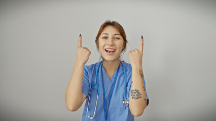 A cheerful young woman nurse with tattoos pointing upwards, isolated on a white background,...