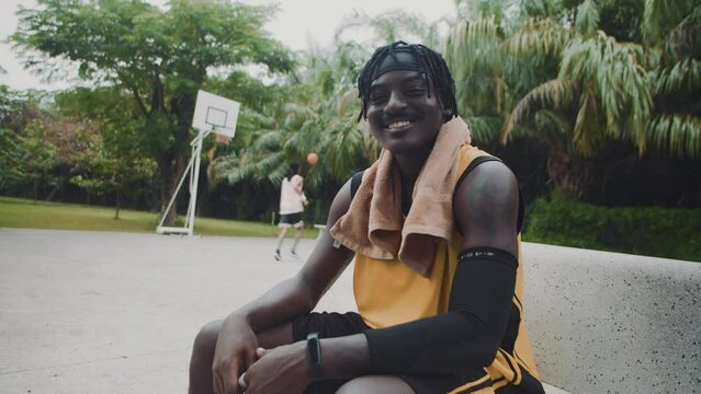 Medium portrait of cheerful black streetball player sitting on bench after training and looking at camera