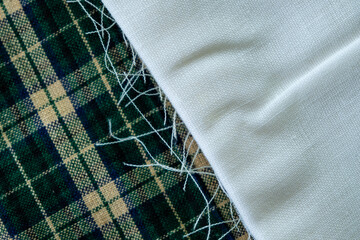 Folded white fabric with frayed edge on top of green plaid