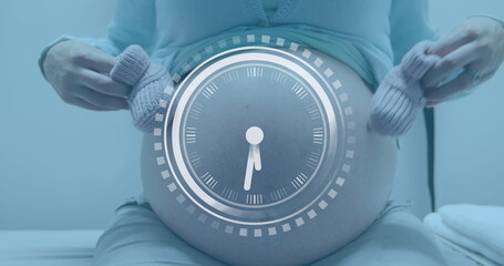 Fast moving clock over midsection of pregnant caucasian woman holding bootees beside belly - obrazy, fototapety, plakaty