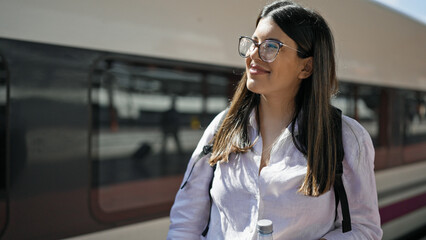 Young beautiful hispanic woman walking down the railway holding bottle of water at train station
