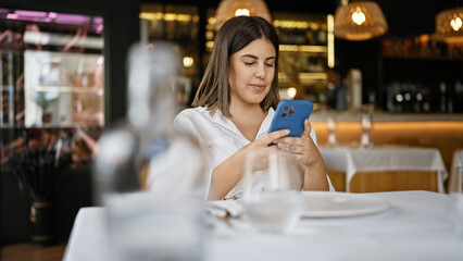 Young beautiful hispanic woman smiling happy using smartphone sitting on the table at the restaurant