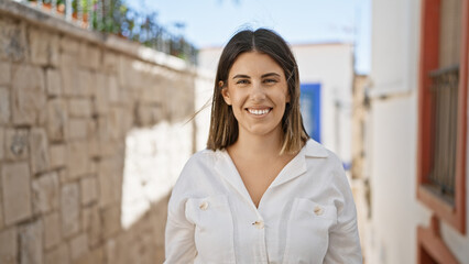 Young beautiful hispanic woman standing smiling at typical spanish old town