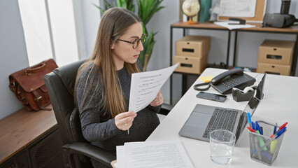 Pregnant hispanic woman reading document in an office setting, symbolizing work-life balance and maternity in the workplace.