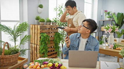 Two men working together in an indoor flower shop, surrounded by plants and floral arrangements.