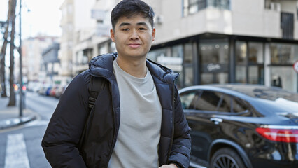 A young asian man stands casually on a busy city street, exuding urban style and confidence.