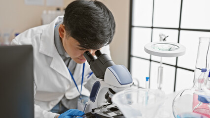 Asian man in lab analyzing samples using microscope in scientific research environment.