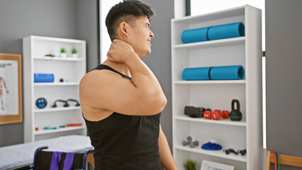 Young asian man experiencing neck pain at a modern rehabilitation clinic's exercise room