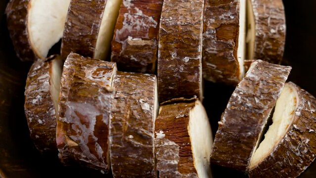 Fresh Cassava root slices with textured brown peel. Raw Yucca ingredient in rustic dish. Starchy Manioc top view. Rotation