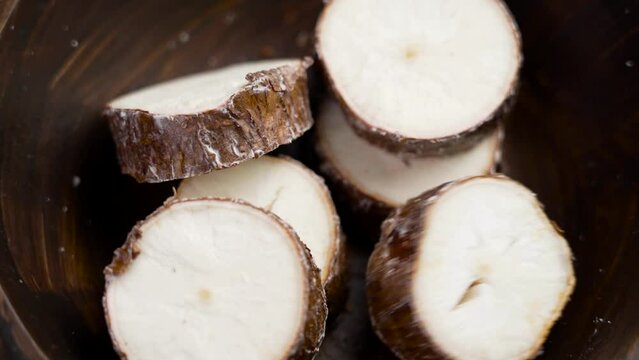 Raw cassava root slices falling into a wooden bowl. Fresh uncooked Yucca tuber. Organic healthy food. Rotation