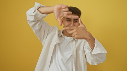 A young adult man gestures framing with hands against a yellow isolated background.