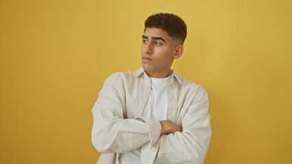 Handsome young man with arms crossed in white shirt against a yellow background, showing a thoughtful expression.