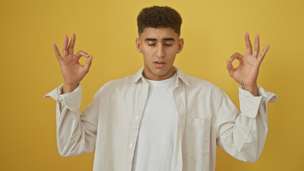 A young man meditates with closed eyes against a yellow background, portraying tranquility and...