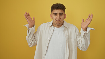 A confused young man shrugging against a yellow isolated background