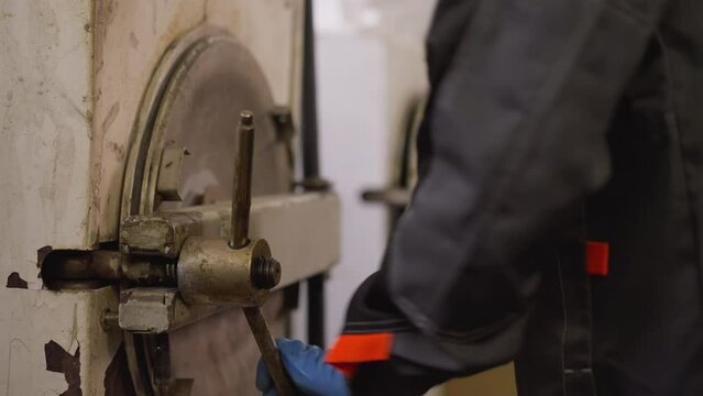 Worker in protective gear manually operating kiln hatch in a ceramic workshop, focus on hand with lever