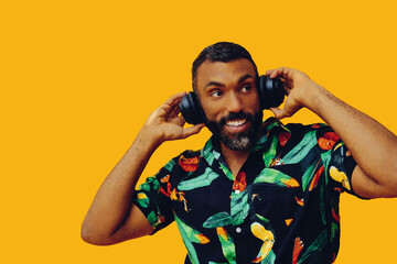 handsome mid adult bearded african american man with headphones posing on yellow background looking away at copy space