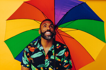 handsome smiling bearded african american man in Hawaiian shirt posing with colorful rainbow umbrella