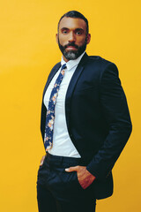 portrait of handsome bearded man in suit and tie, isolated on yellow background hands in pockets