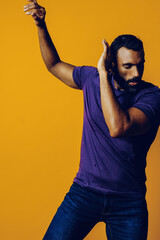 portrait of a handsome sensitive young adult man dancing with purple t-shirt on a yellow background