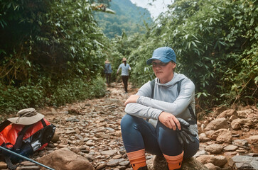 Tired woman hikker resting while trekking with group in wild jungle - 785352079
