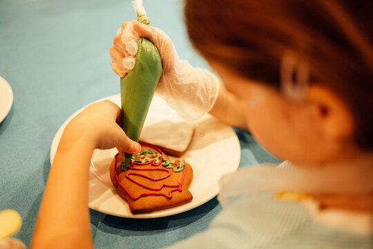 Close-up of a girl painting Christmas cookies with a pastry bag. A girl decorates a ginger yummy with green cream on a blue table.