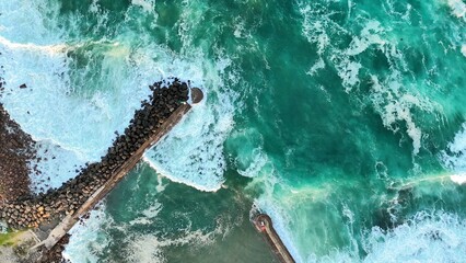 Aerial view of the rugged stormwater break wall with crashing green waves