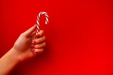 The hand of a young girl with a red manicure holds a candy cane. Cinnamon or peppermint stick on...