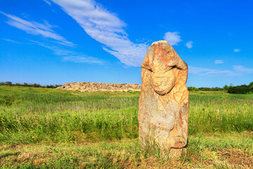 View of the ancient kurgan stela, stone idol against the backdrop of ancient mound of sandstone boulders, in the archeological preserve Kamyana Mohyla, Ukraine