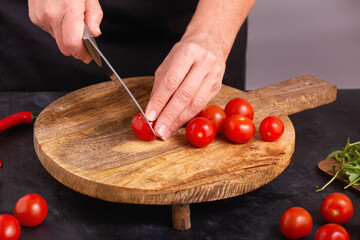 The chef slicing fresh tomatoes for a salad using a large kitchen knife on a wooden chopping board, close-up