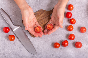 The housewife slicing fresh tomatoes with a large kitchen knife on a wooden chopping board, closeup with selective focus