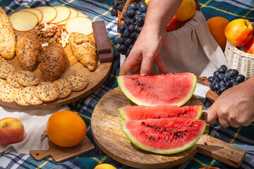 Close-up view of a cut watermelon in hands and laid out food for a picnic, selective focus. The...