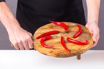 Close-up view of red chili peppers laid out on a cutting board in the hands of a male cook, selective focus