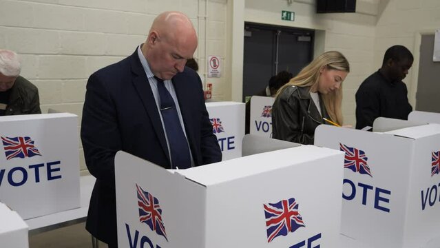 4K: Caucasian Male Voter voting at Polling Place for the UK Election. 50-54 years. People vote at booths. Gimbal up. Stock Video Clip Footage