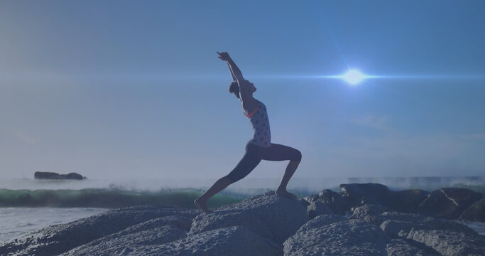 Image of lights over caucasian woman practicing yoga on beach