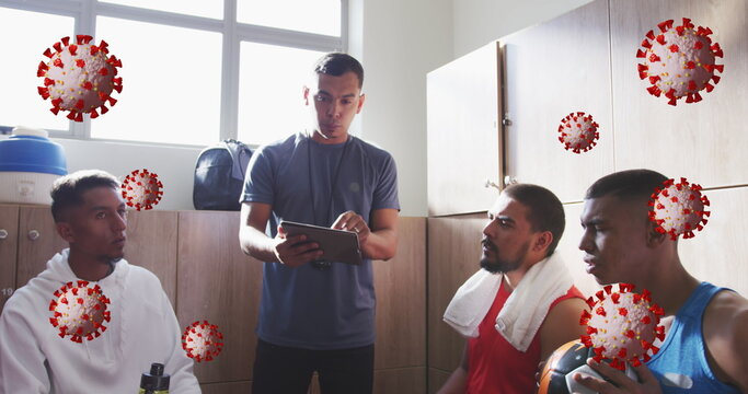 Image of covid-19 cells over male coach discussing with male soccer players in locker room - Powered by Adobe