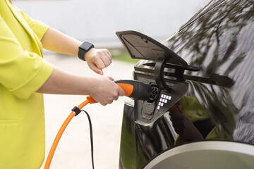 Female plugging an electric car or EV at electric charging station. Woman hands attaching power cable supply to charge electric or EV car using app on wearable smart watch
