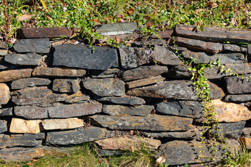 Roadside retaining wall of flat stacked stones, grass and vines above and below, creative nature...