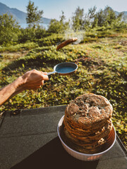 Man cooking pancakes with frying pan outdoor picnic camping summer vacations, vegan healthy food tasty dessert meal - 785384853