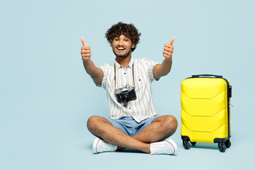 Full body traveler Indian man wear white casual clothes sit near bag show thumb up isolated on...