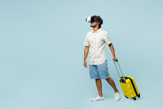Full body traveler man wear white casual clothes hold bag watching in vr headset pc gadget isolated on plain blue background Tourist travel abroad in free time rest getaway Air flight journey concept.