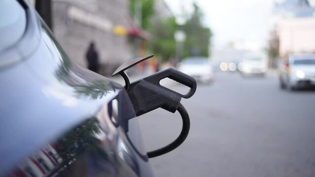 a cable at a city charging station charges an electric car in close-up. i. Plug-in module. the traffic is blurry