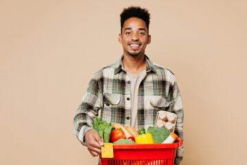 Young smiling happy cheerful man wear grey shirt hold red basket bag with food products give credit...
